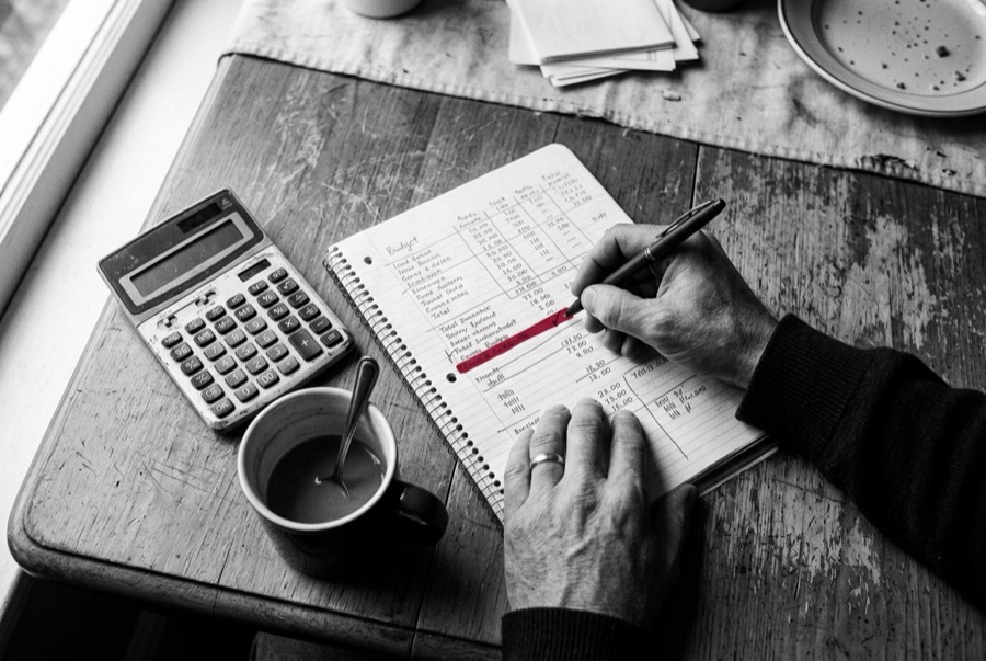 Hands working through a budget in a notebook, with a calculator and a red pen