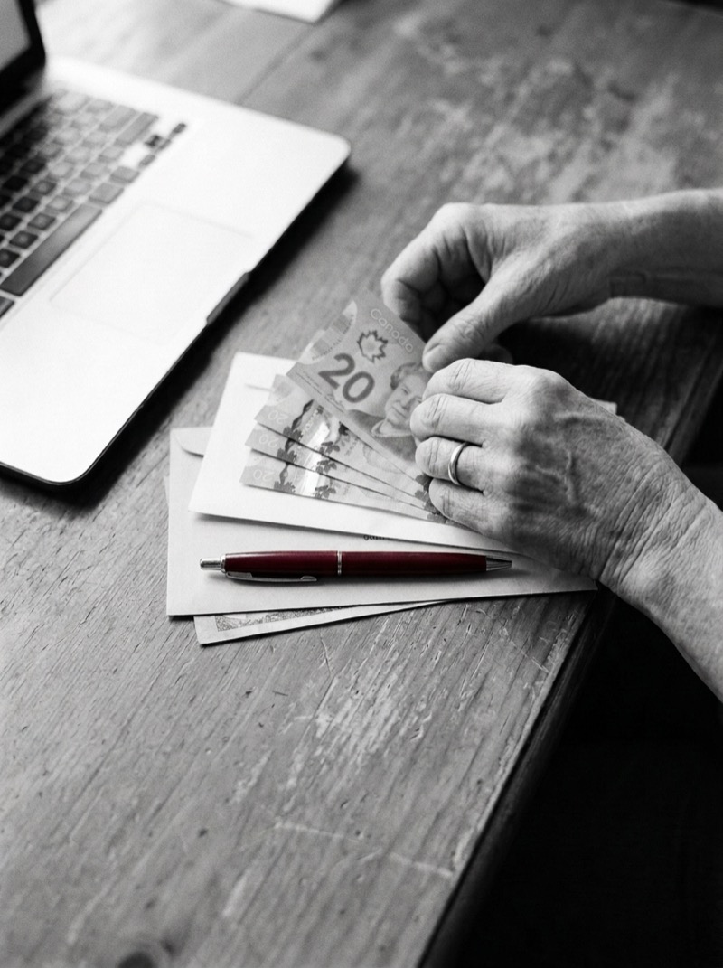 Hands counting cash beside a laptop at a wooden table
