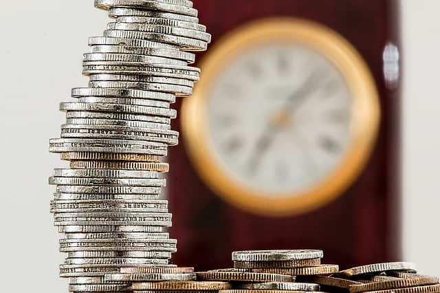 Stacked coins with a blurry clock in the background