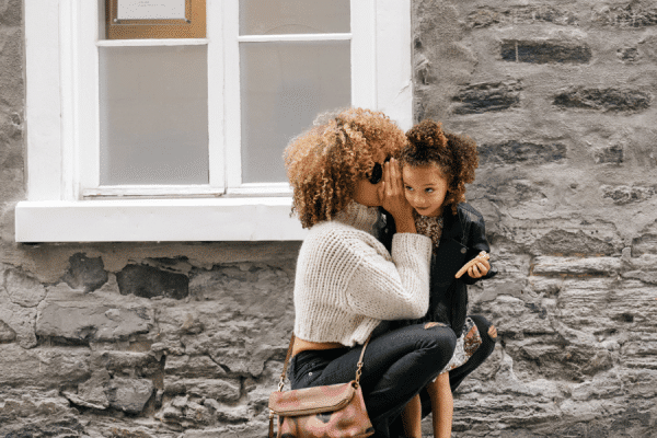 Young lady outside a brick home whispering to a child