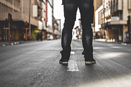 The back of the legs of a person wearing jeans standing in the middle of the street