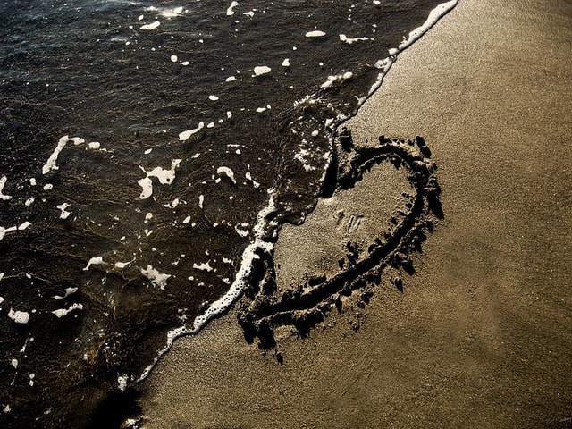 A heart drawn in the sand at the beach getting washed away