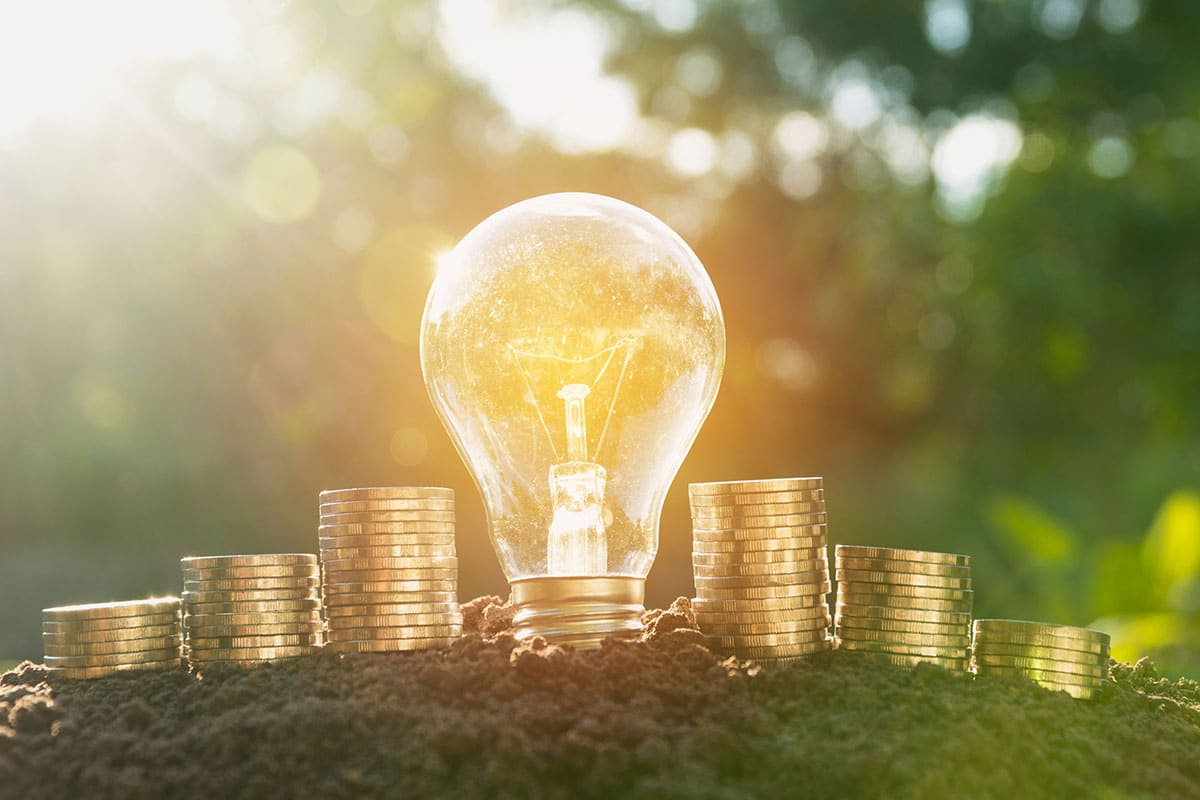 A lightbulb with stacked of gold coins outside