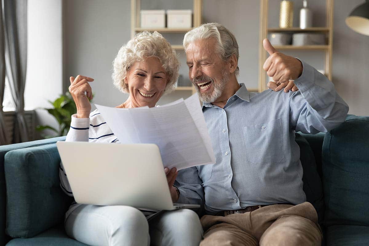 Old couple sitting on the couch happily looking at their paper